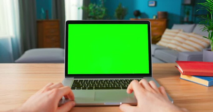 Close up of male Hand is using laptop touch pad. Modern Personal Computer with Mock-up Green Screen Display Standing on the Desk of the Cozy Home. POV view of blank netbook screen.