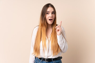 Young caucasian woman isolated on beige background thinking an idea pointing the finger up