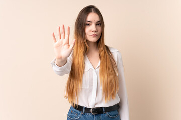 Young caucasian woman isolated on beige background making stop gesture