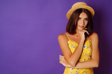 Smiling woman in yellow dress and hat posing purple background. Fashion, style, summer concept. 