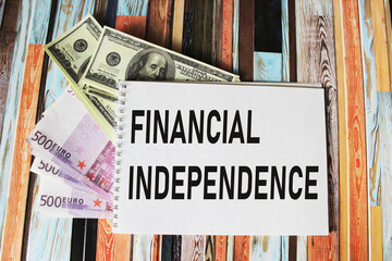 text FINANCIAL INDEPENDENCE concept of financial freedom on a notebook, there are euros and dollars...