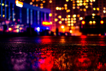 Rainy night in the big city, light from the shop windows and the windows of the house is reflected in the asphalt. View from the level of asphalt