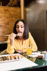 Young Hispanic woman eat sushi in a Japanese food restaurant. Lifestyle dinner for independent and confident friends taking healthy food. Yellow and lavender 2021 year color