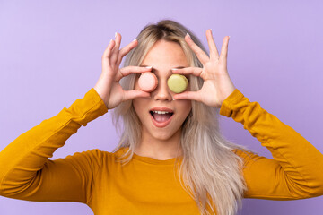 Teenager girl over isolated purple background holding colorful French macarons with surprised expression