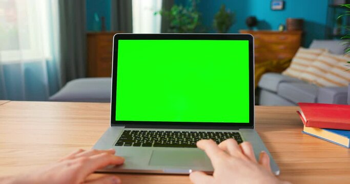 Close up of male Hand is using laptop touch pad. Modern Personal Computer with Mock-up Green Screen Display Standing on the Desk of the Cozy Home.