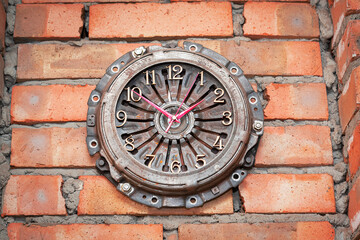 Wall clock from an automobile clutch basket on a brick wall
