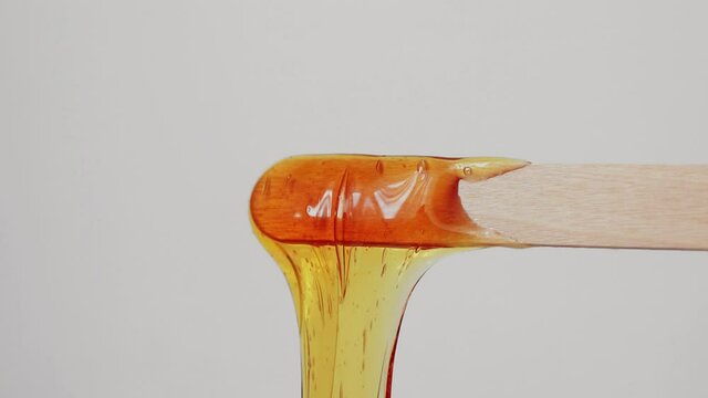 Sugar paste for sugaring flows down from a wooden spatula. Hair removal, epilation, depilation, beauty. Copy space.