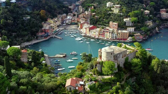 The harbor of Portofino in italy with boats sailing in the water. We can see the city in the middle of forest and mountain near the water - aerial view 4K