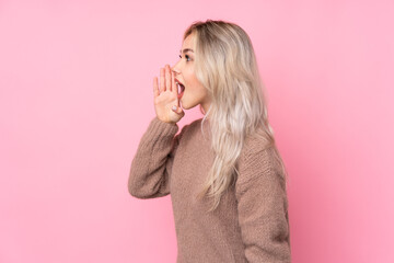 Teenager blonde girl wearing a sweater over isolated pink background shouting with mouth wide open to the lateral