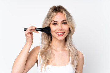 Teenager blonde girl over isolated white background holding makeup brush and whit happy expression