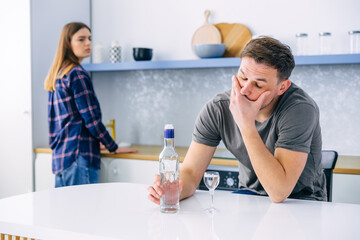 young Caucasian alcoholic sitting with bottle and glass of drink