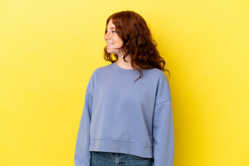 Teenager reddish woman isolated on yellow background looking side