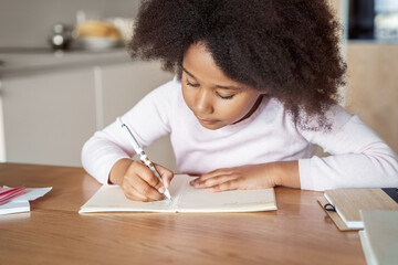 Closeup portrait shot of little mixed-race girl writing in notebook do homework