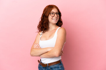 Teenager reddish woman isolated on pink background with arms crossed and happy