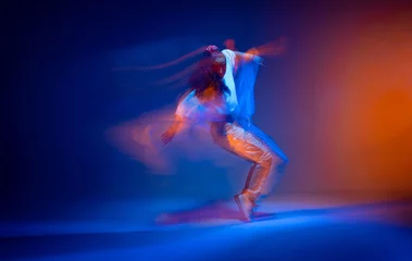 Poster Dancing girl standing on toes in colourful neon studio light. Expressive contemporary hip hop dance. Long exposure © Georgii