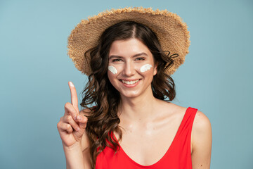 Beautiful, young woman in a straw hat applies sunscreen on her f