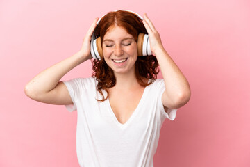 Naklejka premium Teenager reddish woman isolated on pink background listening music