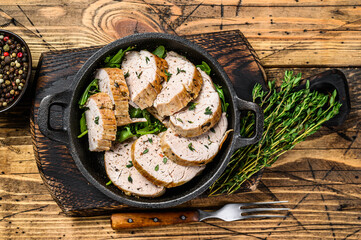 Sliced grilled pork tenderloin steak in a pan. Wooden background. Top view