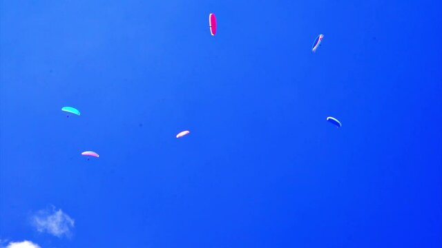 Several paragliders with colorful umbrellas fly in formation on a clear day
