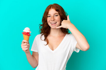 Teenager reddish woman with a cornet ice cream isolated on blue background making phone gesture....