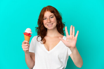 Teenager reddish woman with a cornet ice cream isolated on blue background counting five with fingers