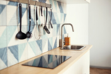 Kitchen spatulas handing on railing on a tiled wall with blue geometric pattern