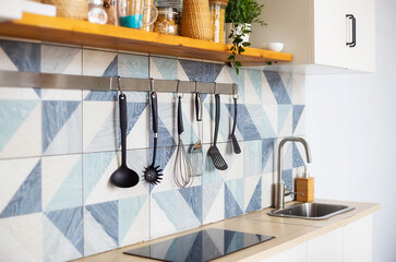 Kitchen spatulas handing on railing on a tiled wall with blue geometric pattern