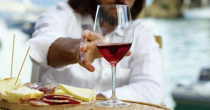 Close up of a man drinking wine and eating cheese in a habor neat the water. He has long brown hair and a white shirt - Red Camera 4K
