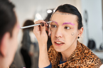 Drag queen sitting in front of the mirror and painting his brows