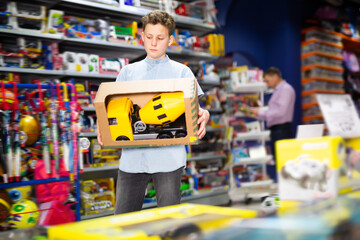 Glad teenage boy choosing toy cement mixer machine in modern toy store