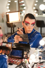 Drag queen looking at the mirror and applying blushes at his face