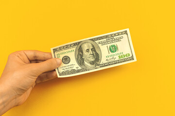 Man hand hold one hundred dollar bill on yellow background of office table, concept of banking deposit