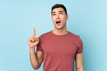 Young caucasian handsome man isolated on blue background pointing up and surprised