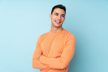 Young caucasian handsome man isolated on blue background with arms crossed and happy