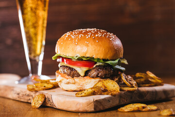 Classical Cheese burger with potato wedges and glass of beer on a wooden board with dark brown...
