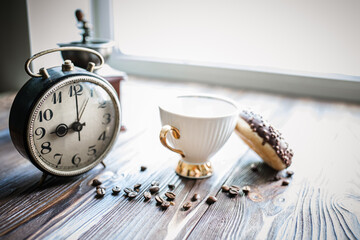 vintage alarm clock showing 9am on the table next to a cup of coffee and a doughnut. Breakfast....
