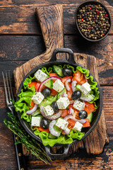 Greek salad with fresh vegetables and feta cheese in a pan. Dark Wooden background. Top view