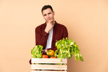 Farmer with freshly picked vegetables in a box isolated on beige background thinking