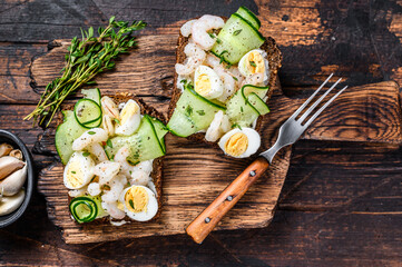 Sandwiches with shrimp, prawns, quail eggs and cucumber on rye bread. Dark Wooden background. top...