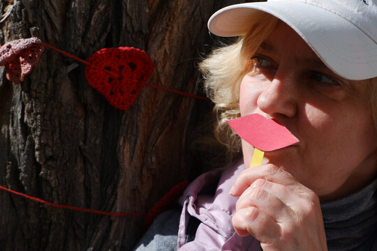 A woman with garlands of hearts holds paper lips and a heart as a symbol of love. World Kiss Day.