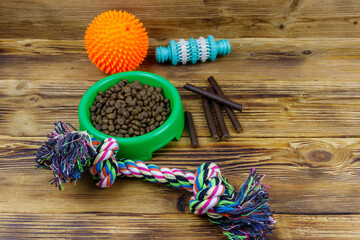 Dog toys and feed for dogs in green plastic bowl on wooden background. Dog care concept