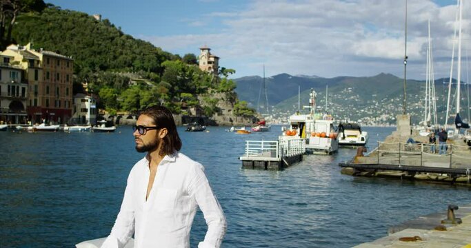Handsome man walking in the port of Portofino under the sunlight.He has long brown hair and a white shirt - Red Camera 4K