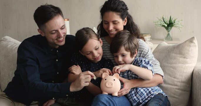Young couple preschool son little daughter sit on sofa dropping coins into piggy bank. Happy family saving money for new housing, dream, education of children in future. Teach kids be thrifty concept
