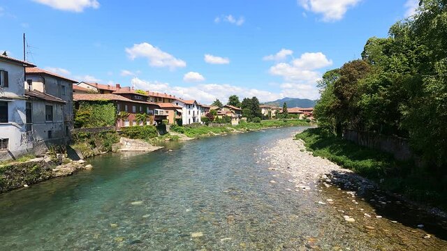 The water of a river flows fast between the houses under a blue sky