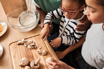 Father helping to his daughter chopping mushrooms for the pizza
