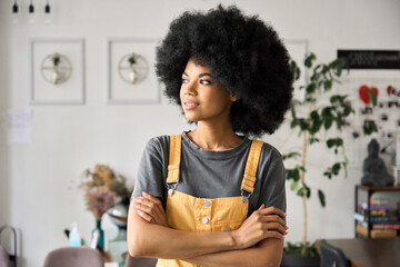 Young confident generation z black mixed race hipster businesswoman standing with arms crossed looking away in restaurant or cafe. Small business entrepreneurship concept. - obrazy, fototapety, plakaty