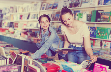 Fototapeta na wymiar Portrait of smiling woman with teen girl picking textbooks for school in book shop