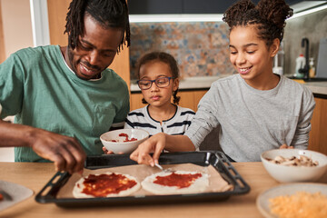 Sisters putting stuffing to the pizza laying at the baking sheet