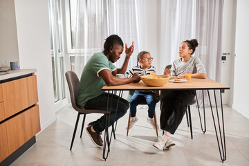 Children having breakfast with appetite and looking into their father