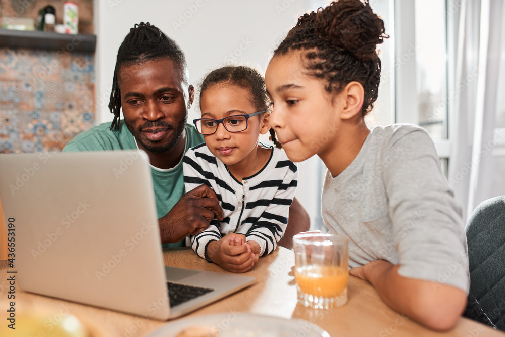 Wall mural sisters watching cartoons at the laptop wit their father while having breakfast